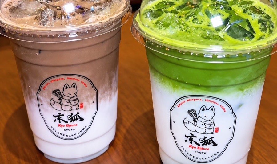 Iced hojicha latte and iced matcha latte side by side in clear Kyo Kitsune cups, each layered over milk and stamped with the fox emblem